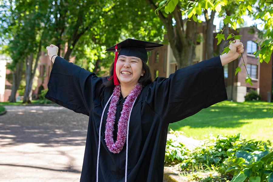 Student celebrating with arms up, graduation gown on